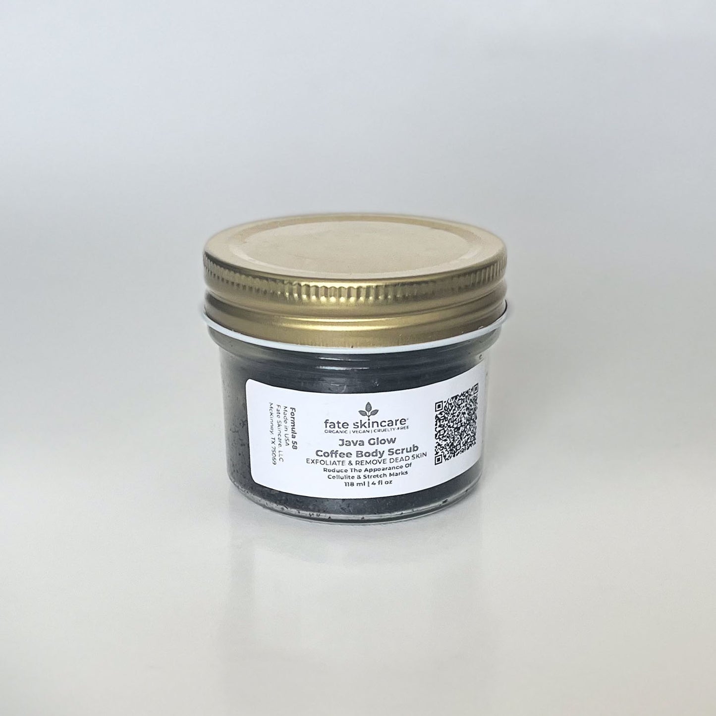 Fate Skincare's Java Glow Coffee Body Scrub in a clear glass jar with a brass lid, featuring a rectangular label displaying the product name and company logo.