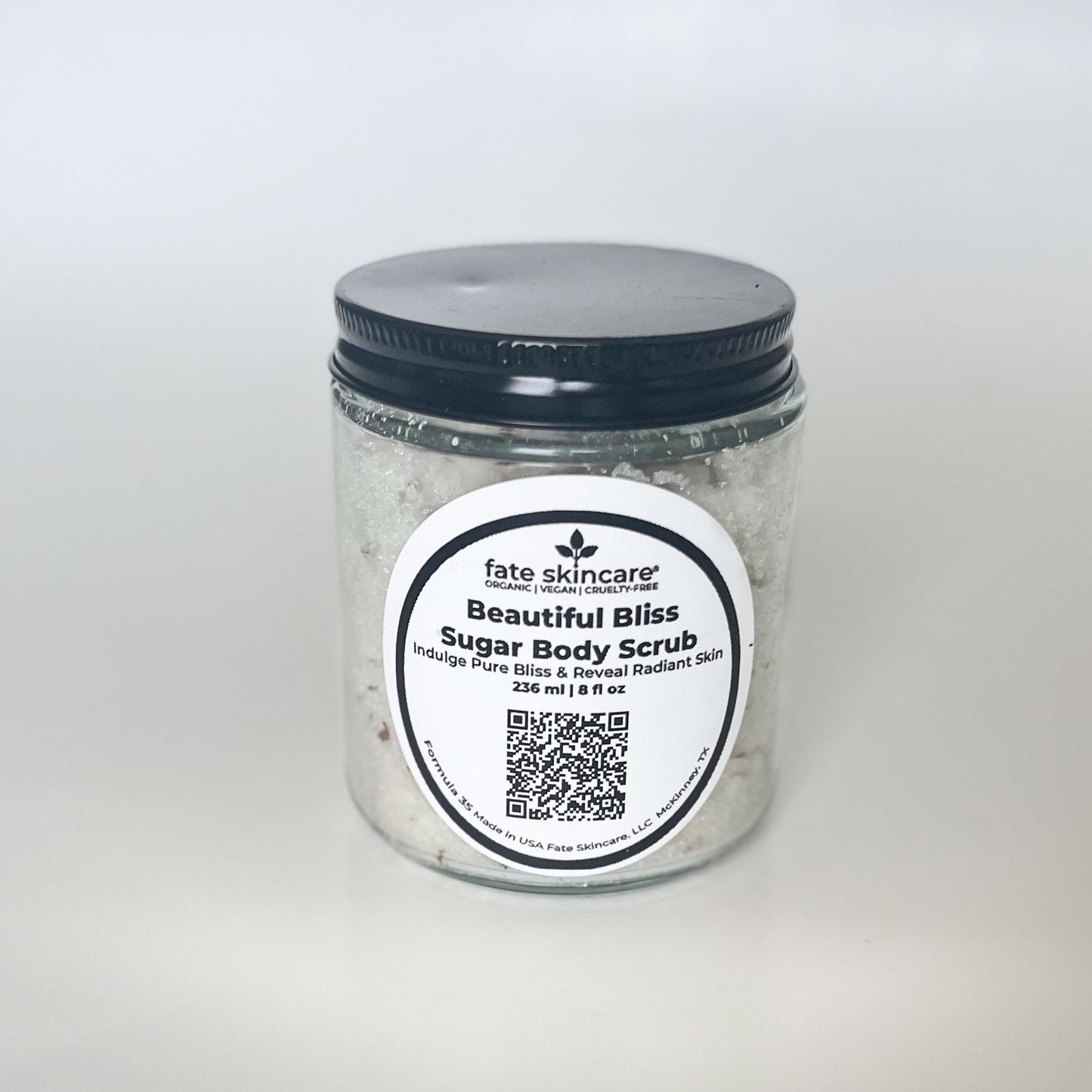 Fate Skincare's Beautiful Bliss Sugar Body Scrub in a clear glass jar with a black lid, featuring a round label displaying the product name and company logo.