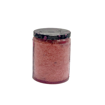 A clear glass jar with a black floral-patterned lid, showing a textured pink scrub inside.