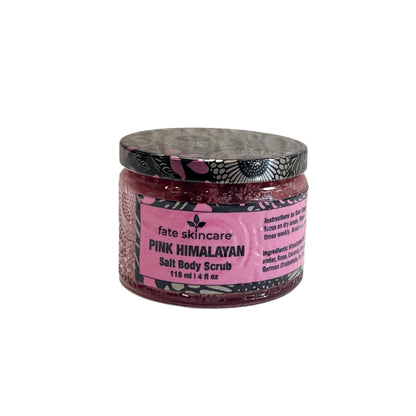 A clear glass jar of "Fate Skincare Pink Himalayan Salt Body Scrub" with a black and pink patterned lid, placed on a white surface with a textured white background. The pink label indicates that the scrub contains Himalayan pink salt and nourishing oils.