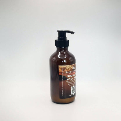 Fate Skincare's Suds-less Body Wash in a 8 ounce glass amber bottle equipped with a black pump dispenser. The label prominently displays the product's name in white extra-bold letters against a background of a golden sky.