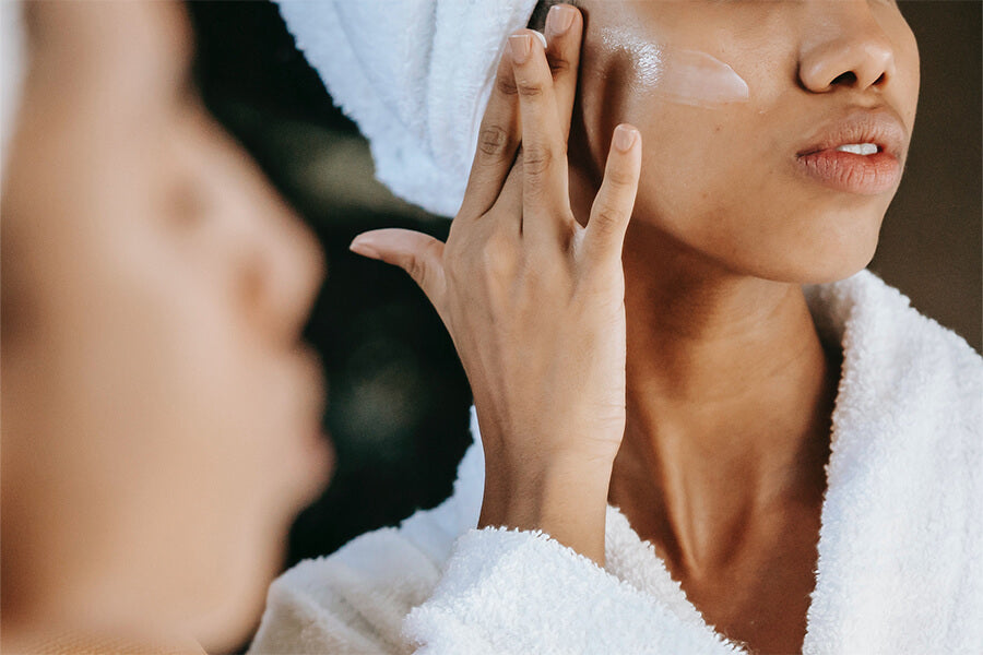 Image of Mimi applying Fate Skincare's Healing Beauty Balm onto her face, reflecting in the mirror, following the use of the foaming mousse facial cleanser.